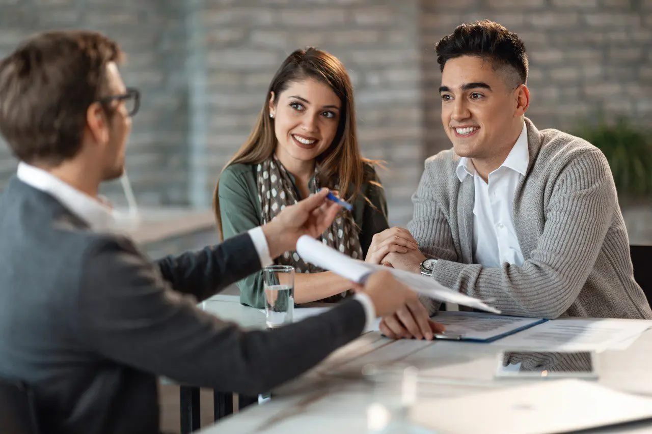 Happy couple having a meeting with bank manager who he is offering them to sign a contract.